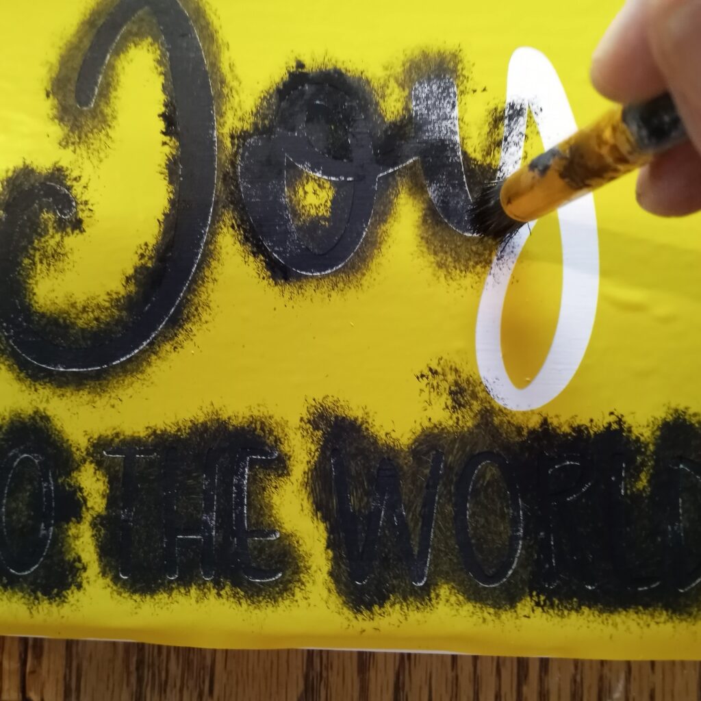 Using a stencil brush to paint a Joy to the World sign on scrap wood