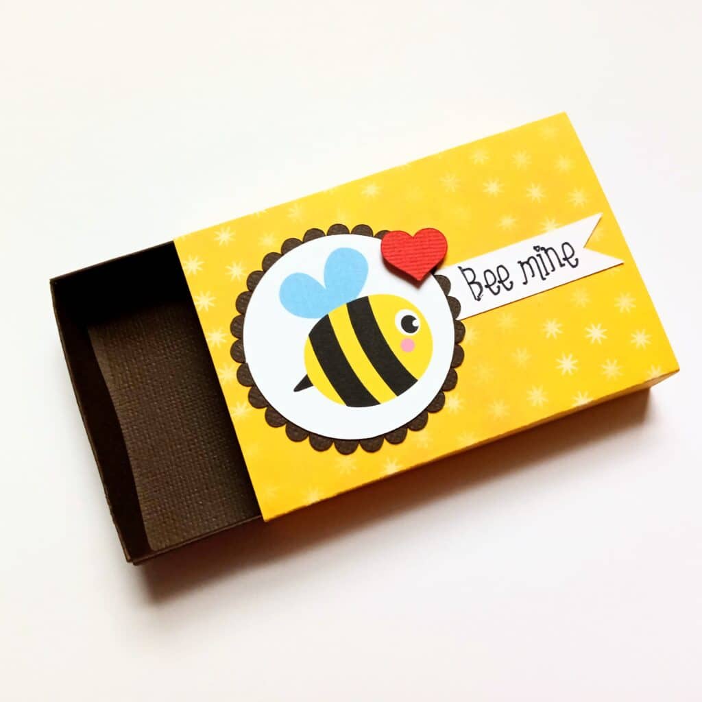 Adorable 'Bee Mine' matchbox featuring charming bee-themed designs, a perfect Valentine's Day gift or gesture of love. The whimsical illustration adds a touch of sweetness to this delightful and thoughtful creation.